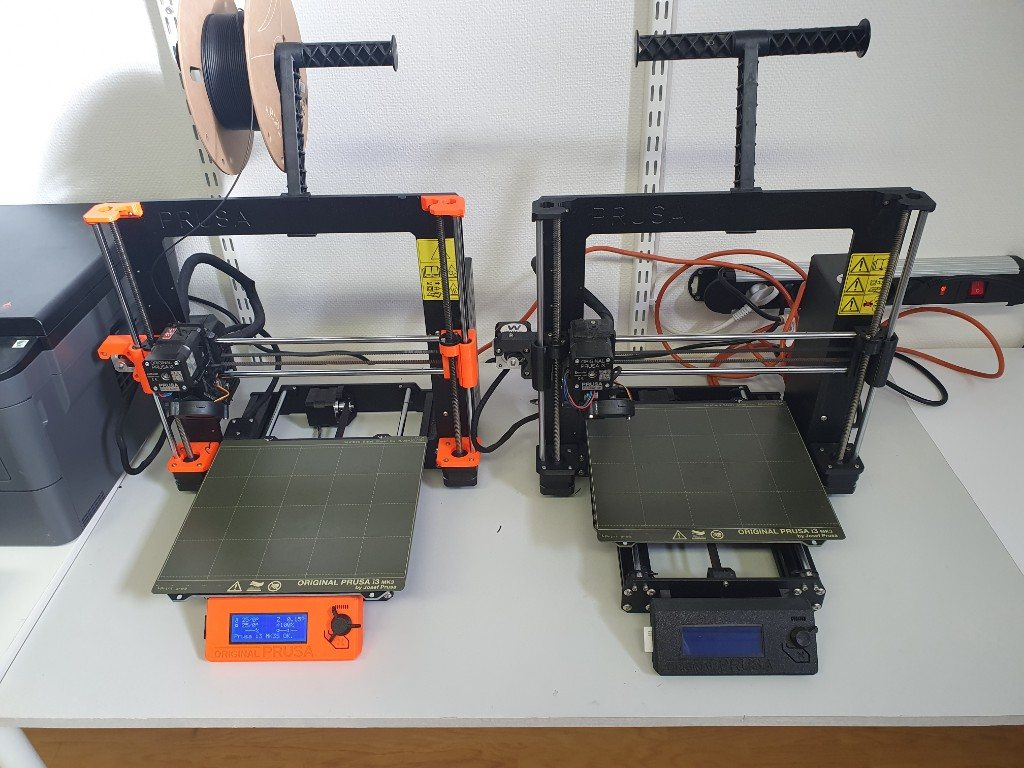 Två Original Prusa i3 MK3, en med orange detaljer och en svart